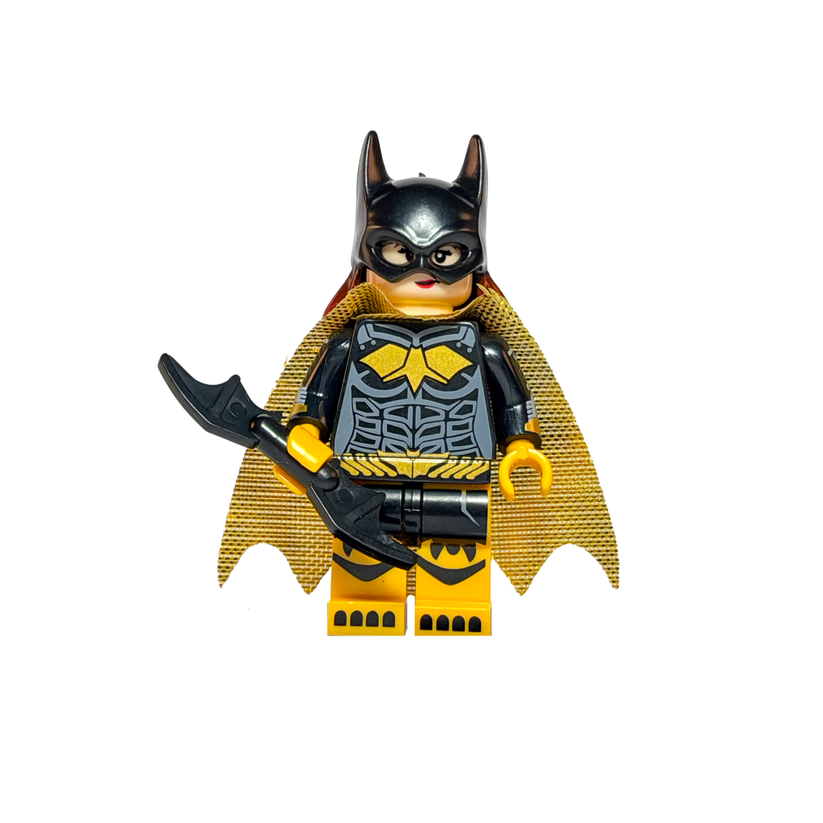 Minifigura de colección de Batichica (Batgirl) de DC Comics sobre un fondo blanco puro. Viste un traje negro con un logo de murciélago amarillo y botas amarillas. Tiene una capa dorada brillante y el pelo largo pelirrojo asomando bajo su máscara negra. Sostiene un Batarang negro en su mano derecha y está parada sobre una base negra.