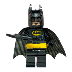 Minifigura de colección de Batman de DC Comics sobre un fondo blanco puro. Viste un traje negro con un cinturón amarillo brillante y el logo del murciélago amarillo en el pecho. Tiene una capa de tela negra y sostiene un Batarang negro en su mano derecha. Está parado sobre una base de exposición negra cuadrada.