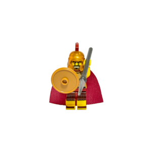 Minifigura de un guerrero espartano sobre un fondo negro. Viste una capa de tela roja y una armadura ligera con detalles de cuero. Lleva un casco dorado brillante con una cresta roja superior. Sostiene un escudo circular dorado en su mano derecha y una lanza plateada en la izquierda. La iluminación resalta los reflejos metálicos del casco y el escudo contra el fondo oscuro.