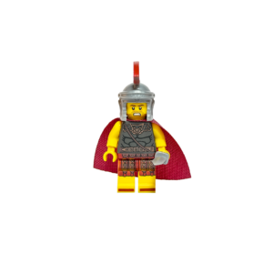 Minifigura de un comandante romano sobre un fondo negro. Viste una armadura gris oscuro con detalles de correas de cuero rojas y una capa de tela roja vibrante. Lleva un casco plateado con una cresta roja transversal. Su rostro tiene una expresión de mando con barba. Sostiene una espada corta plateada en su mano izquierda. La iluminación resalta la textura de la capa y el brillo del casco contra el fondo oscuro.