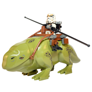 Figura de colección a gran escala de un Dewback verde de Star Wars montado por un Sandtrooper, sobre un fondo negro puro. El gran reptil tiene manchas oscuras y lleva una montura marrón con riendas. El soldado tiene armadura blanca con marcas de arena, una mochila en la espalda y sostiene una vara larga negra. Un rifle bláster cuelga de un lado de la montura.