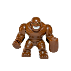 Minifigura de colección de Cara de Barro (Clayface) de DC Comics sobre un fondo blanco puro. La figura es de color marrón con una textura que simula barro derretido. Su brazo derecho termina en una maza grande y redonda del mismo material. Tiene ojos amarillos brillantes y una boca abierta mostrando dientes, con una expresión monstruosa.